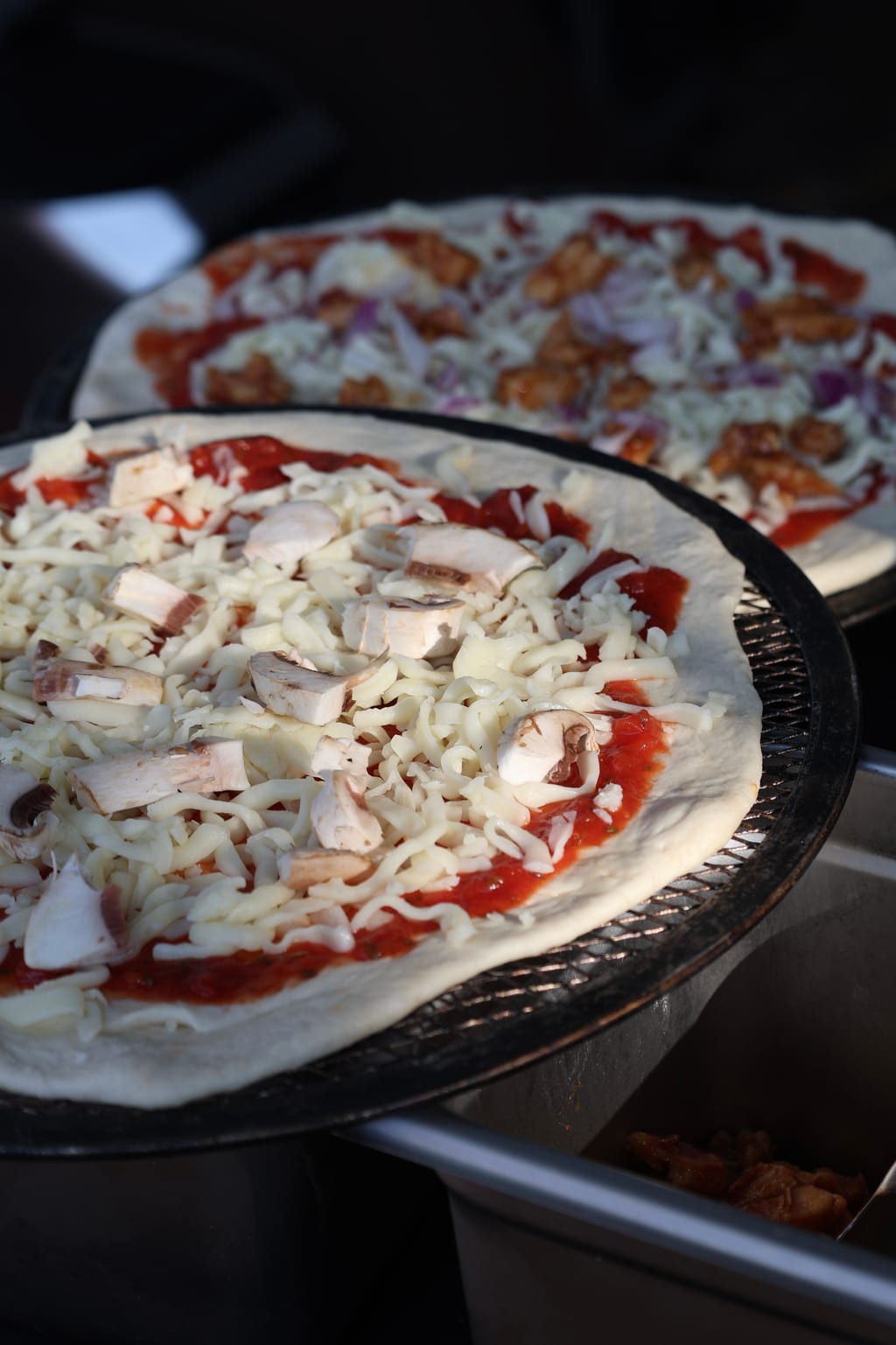 Two pizzas being built side-by-side — BBQ chicken and mushroom prep at a Toronto catering event